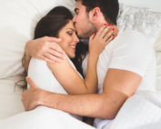 Couple se câlinant amoureusement. L'homme embrasse le front de la femme allongé dans un lit