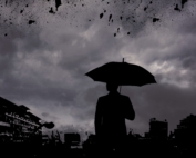 Silhouette d'un homme de dos tenant un parapluie sous un ciel gris foncé
