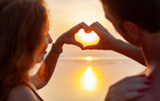 Jeune couple formant un cœurs avec leur mains, avec un couché de soleil en arrière plan