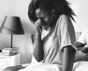 femme assise sur un lit qui à la main sur le visage et semble pleurer