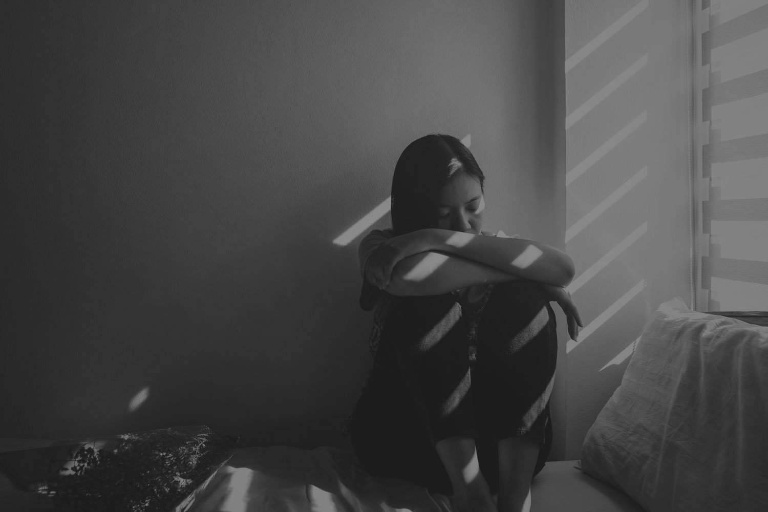 Image en noir et blanc avec une jeune fille assise qui tient ses genoux contre sa poitrine et a l'air triste.
